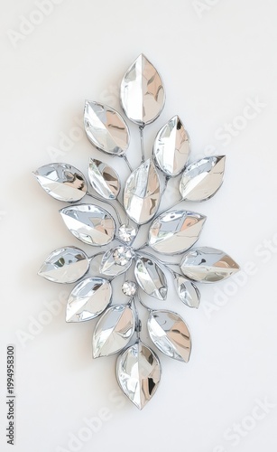 Decorative silver metal wall art piece with glittering crystal accents forming an abstract organic leaf design, reflecting light against a white background, symbolizing elegance and luxury