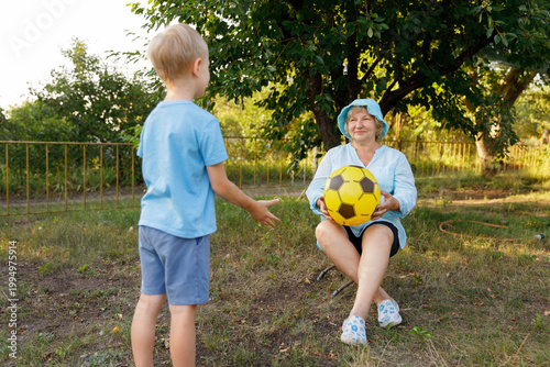 Mature woman sitting in garden and holding yellow ball for grandson.