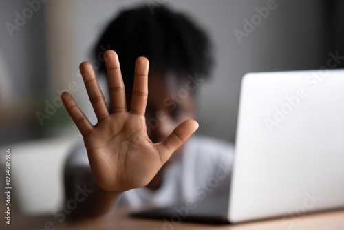 Child raising a hand to stop while sitting behind a laptop, ideal for online privacy, cyber safety, and digital boundaries content