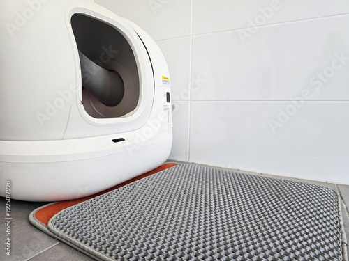 Modern automatic self-cleaning cat litter box placed on a tiled floor with a mat. Concepts of pet care technology, home convenience, and smart living solutions.