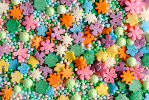 Colorful top down view sugar sprinkles shaped like flowers and stars mixed with small round pastel beads.