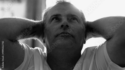 Fotografie Middle-aged man resting with eyes closed, hands behind head, in soft daylight, e
