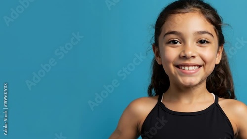 Portrait of a smiling young girl on a blue background. Happy child with brown hair and eyes in studio. Happiness and childhood concept. Copy space for text