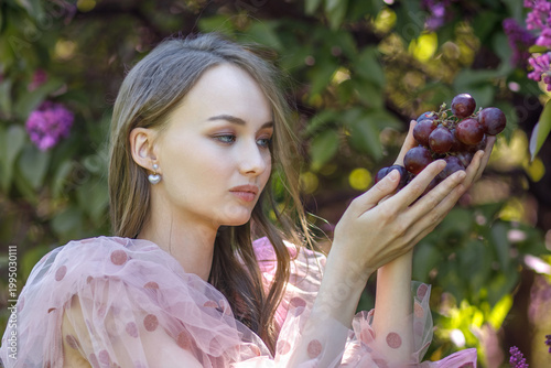 Portrait of a young woman with long hair in a pink dress among blooming lilacs. Spring blossom