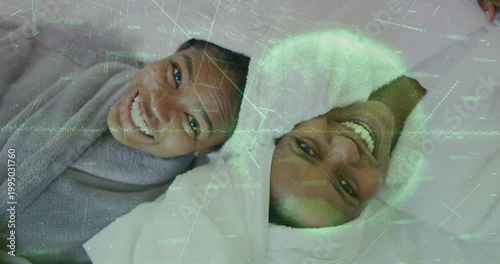 Smiling mother and daughter lying on bed in bedroom, wearing towels with holographic overlay