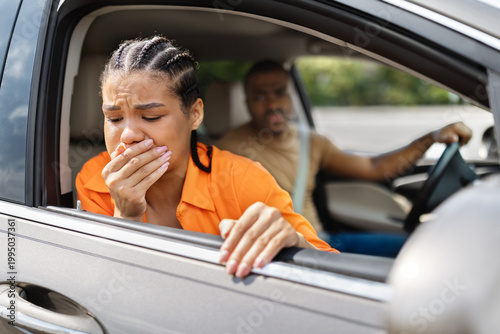 Obraz na płótnie Young Black woman feeling carsick leaning out open car window, concerned man dri