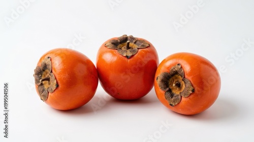 Three ripe orange persimmons isolated on a white background, healthy autumn fruit for nutrition, grocery, vegetarian diet and seasonal produce themes, smooth skin and distinctive calyx arranged in a