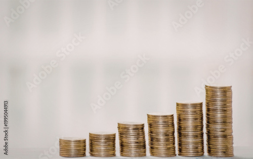 Stacks of gold coins rising in height on a light gray background symbolizing financial growth and investment