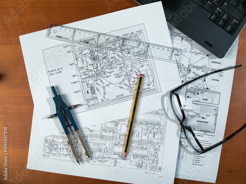 Engineering Plans and Glasses Zenith - Overhead view of technical schematics and blueprints on a desk with glasses, a laptop, and a smartphone, symbolizing hard work and planning.