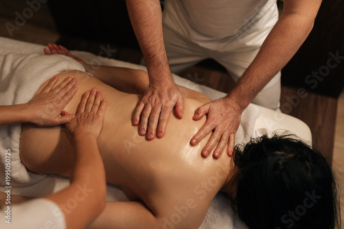 Quadro su tela Close-up hands of male and female professional masseurs performing relaxing four hand massage on woman back, using warm oil in dark wellness center for deep muscle relief and rejuvenation body care