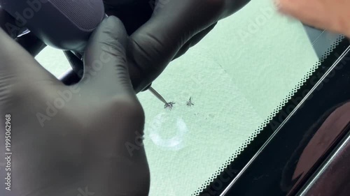 Windshield repair. Repair of a chip on the windshield of a car. Mounted windshield repair bridge holds resin applicators securely over the crack. Bridge tool for injecting resin in damaged windshield.