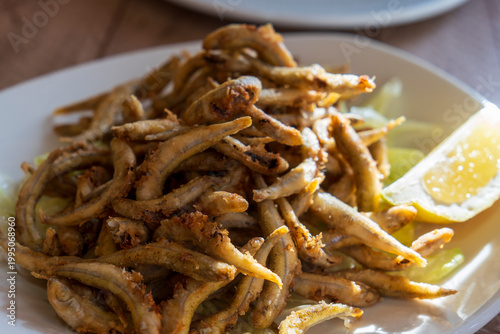 Small fried fish with lemon on white plate served as appetizer or tapa in bar Spain pescaditos dish
