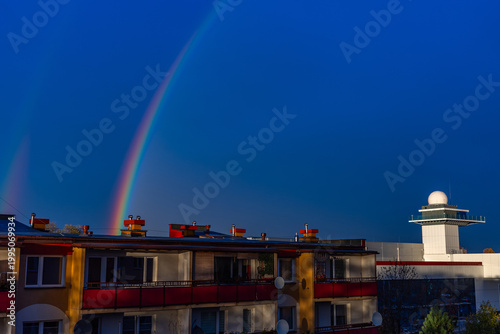A colorful rainbow over apartment buildings against a dark blue sky. Dark skies after a storm.