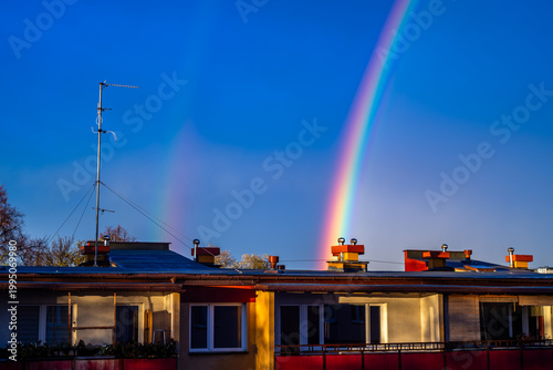 A colorful rainbow over apartment buildings against a dark blue sky. Dark skies after a storm.