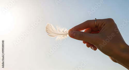 Hand holding delicate white feather against clear blue sky background
