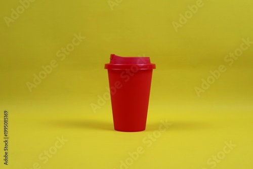 Red plastic coffee cup with lid on a yellow background, minimal studio composition representing takeaway coffee concept.