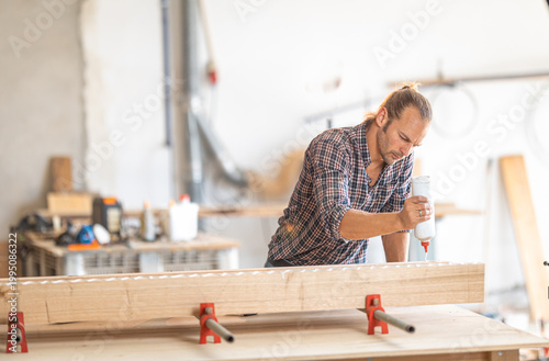 Woodworker applying glue to wood plank in workshop
