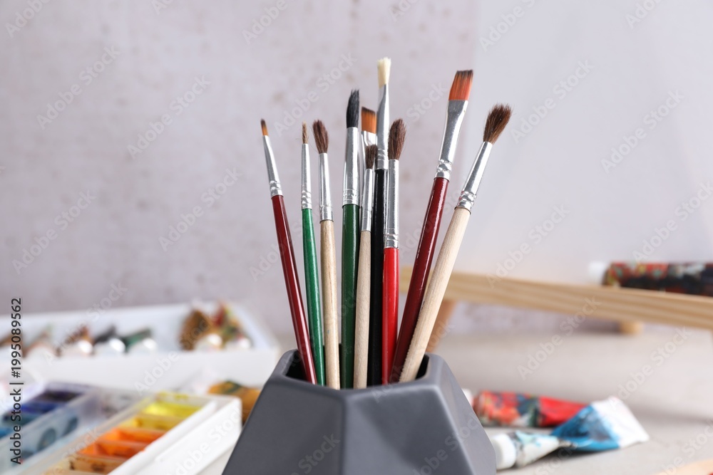 Fototapeta premium Paintbrushes in holder and paints on light table, closeup