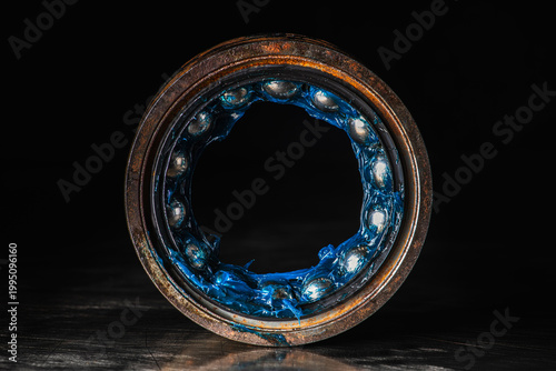 Old ball bearing covered in grease placed on a metal surface with visible reflection. Lubrication, mechanical maintenance, wear, and machine components