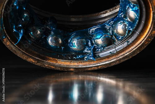 Old ball bearing covered in grease placed on a metal surface with visible reflection. Lubrication, mechanical maintenance, wear, and machine components