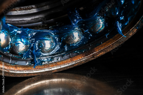 Old ball bearing covered in grease placed on a metal surface with visible reflection. Lubrication, mechanical maintenance, wear, and machine components
