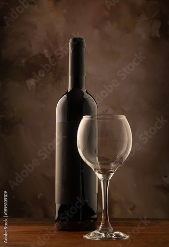 Bottle and wine glass, bottle and wine glass on a rustic wooden surface and abstract background, low key photo, selective focus.