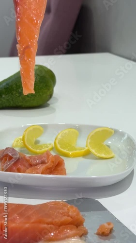 Male hands slicing salmon on white plate lemon tomato avocado healthy food preparation closeup