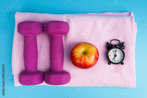 Foto Healthy lifestyle and fitness routine concept with dumbbells, apple, and alarm clock on towel, symbolizing exercise, diet, time management, weight loss, and overall wellness