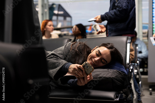 Bild auf Leinwand Smiling girl lays down in airport, using mobile phone to chat with family, arriving home for holidays