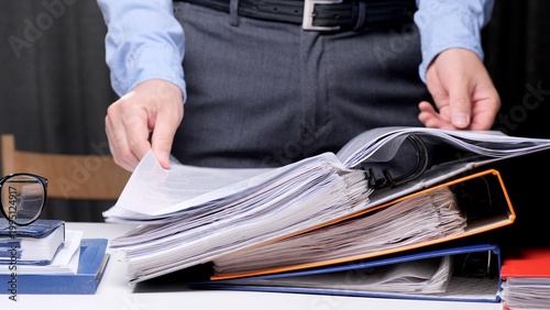 Fotografía Person standing at a desk and reviewing a document in an open binder, performing