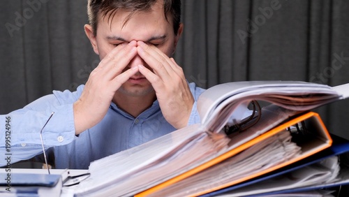 Photos Overwhelmed male office worker rubbing his temples at a cluttered desk, exhauste