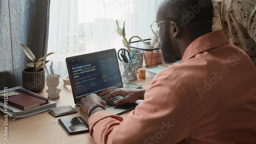 Medium rear shot of young African American husband and wife choosing travel dates on flight booking website on laptop, while preparing to purchase tickets for summer holidays overseas