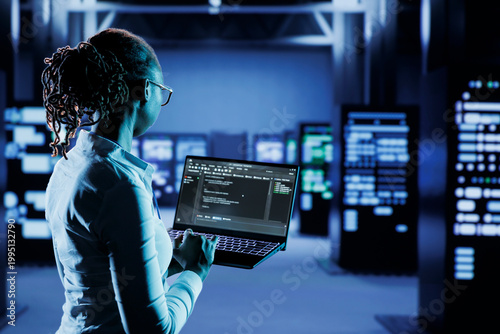Experienced specialist running code and programming on laptop, troubleshooting and upgrading high tech facility designed to accommodate multiple clusters of fully operational server cabinets