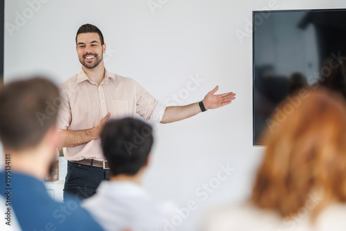 Man gives a presentation in a modern office while an audience listens and engages during a corporate training session