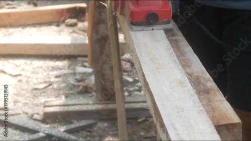 A woodworker uses an electric planer to smooth the surface of a wooden beam on a building construction project.