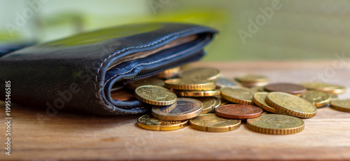 An old wallet with scattered coins on a blurry background.