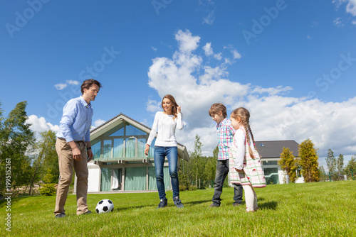 Foto Family playing soccer on lawn in front of modern house