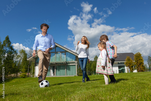 Family playing soccer on lawn in front of modern house