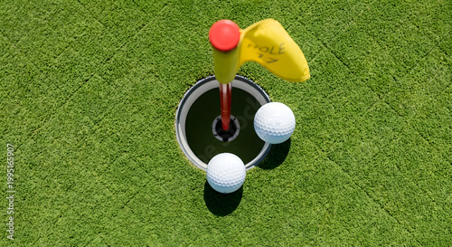 A high-angle view of two golf balls resting on the edge of a vibrant green cup with a yellow flag numbered seventeen on a sunny day. Generative AI