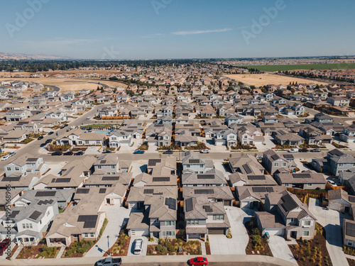 Fotografía Aerial Planned Grid Community Long Perspective Revealing Symmetric Rows Of Houses, Narrow Backyards, Parked Cars, Distant Farmland, Serene Afternoon Light And Efficient Street Layout