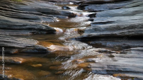 A serene natural stream carves its way through ancient, layered rock formations, showcasing the timeless power and beauty of erosion in a tranquil wilderness setting