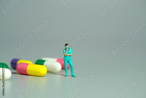 Miniature people toy figure photography. A men doctor or nurse thinking in front of medicine pills. Isolated grey background