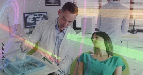 Leaning dentist in lab coat examining reclining patient in green top, dental chair with chart xray