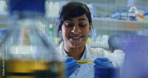 Smiling scientist in white lab coat blue gloves holding test tube at bench, showing data overlay