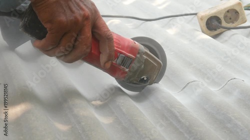 A construction worker uses a hand grinder to cut asbestos or fiber cement roofing sheets.