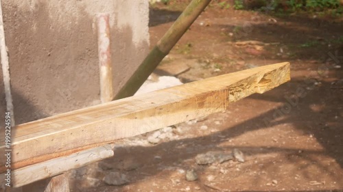 A woodworker uses an electric planer to smooth the surface of a wooden beam on a building construction project.