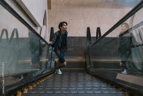 Fotografía Young man riding a modern escalator in an urban building, looking up with curios