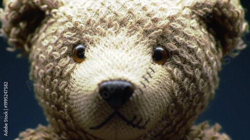 A close-up of a vintage, knitted teddy bear with a shiny eye, detailed stitching and a textured surface