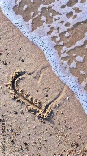 Heart drawn in sand washed by ocean wave, love and romance concept.