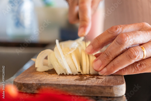 Close-up of Senior Woman Hands Slicing White Onion on Wooden Cutting Board